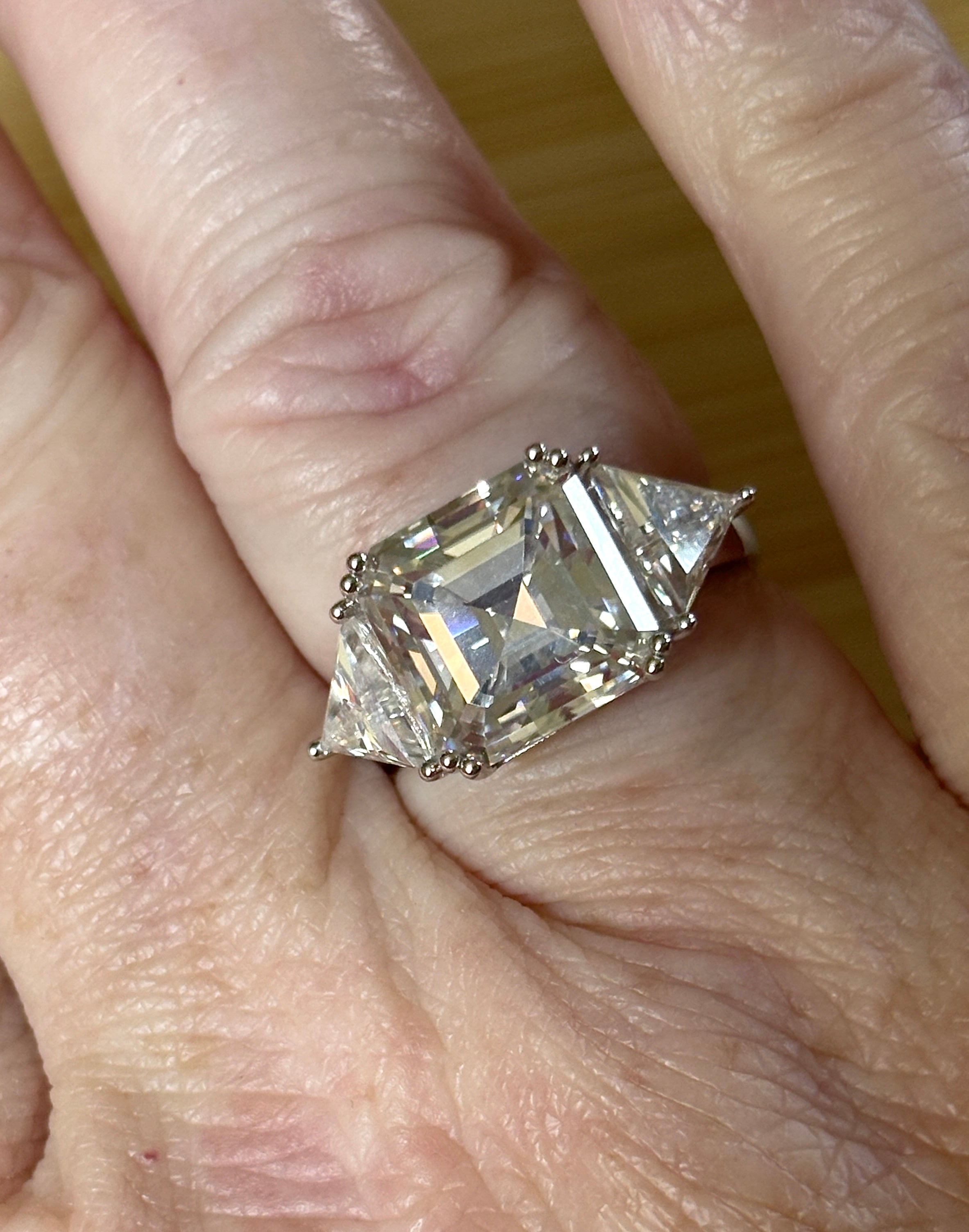 A 9.4cttw Moissanite statement ring with a 7ct Asscher-cut center stone and (2) 1.20ct Moissanite trillions, with bright 14k white rhodium!
