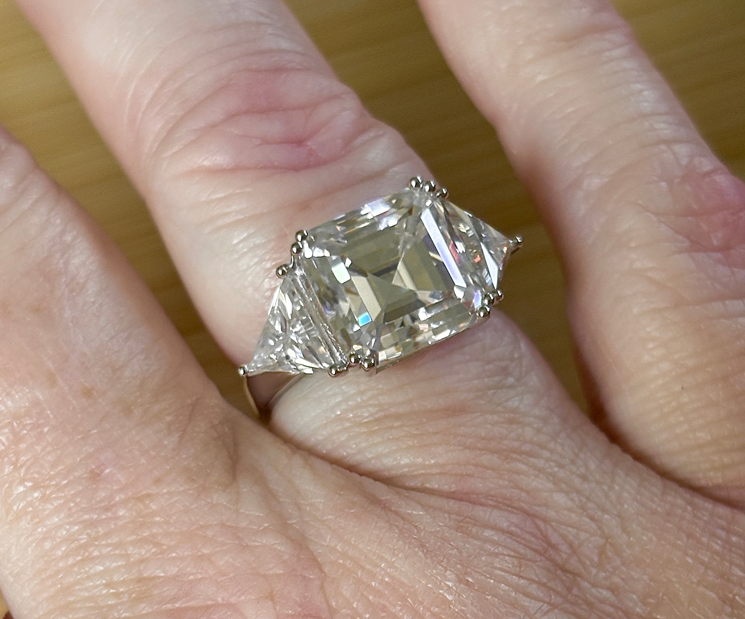 A 9.4cttw Moissanite statement ring with a 7ct Asscher-cut center stone and (2) 1.20ct Moissanite trillions, with bright 14k white rhodium!