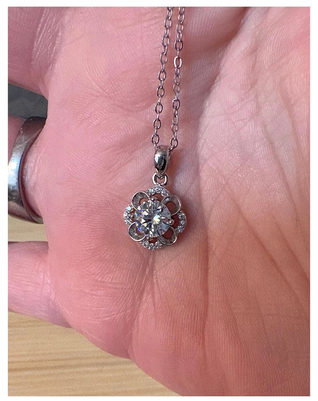 Moissanite necklace. With a floral motif, this pendant features a 1ct Moissanite nestled within alternating “petals” of silver and zircons!