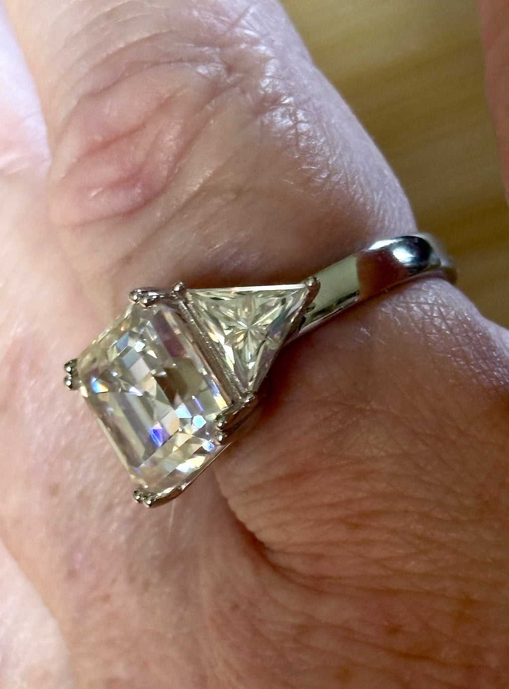 A 9.4cttw Moissanite statement ring with a 7ct Asscher-cut center stone and (2) 1.20ct Moissanite trillions, with bright 14k white rhodium!