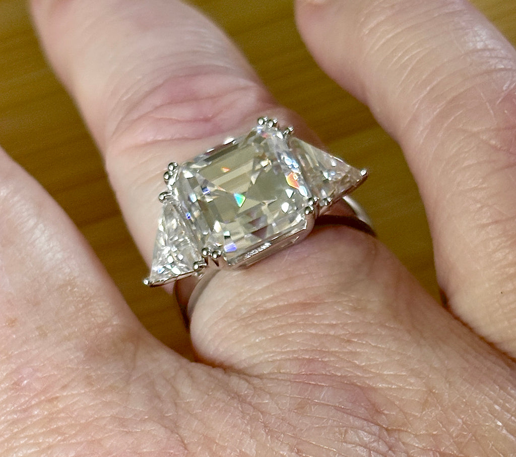 A 9.4cttw Moissanite statement ring with a 7ct Asscher-cut center stone and (2) 1.20ct Moissanite trillions, with bright 14k white rhodium!