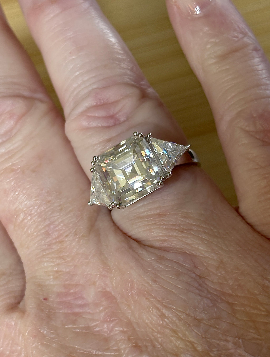 A 9.4cttw Moissanite statement ring with a 7ct Asscher-cut center stone and (2) 1.20ct Moissanite trillions, with bright 14k white rhodium!