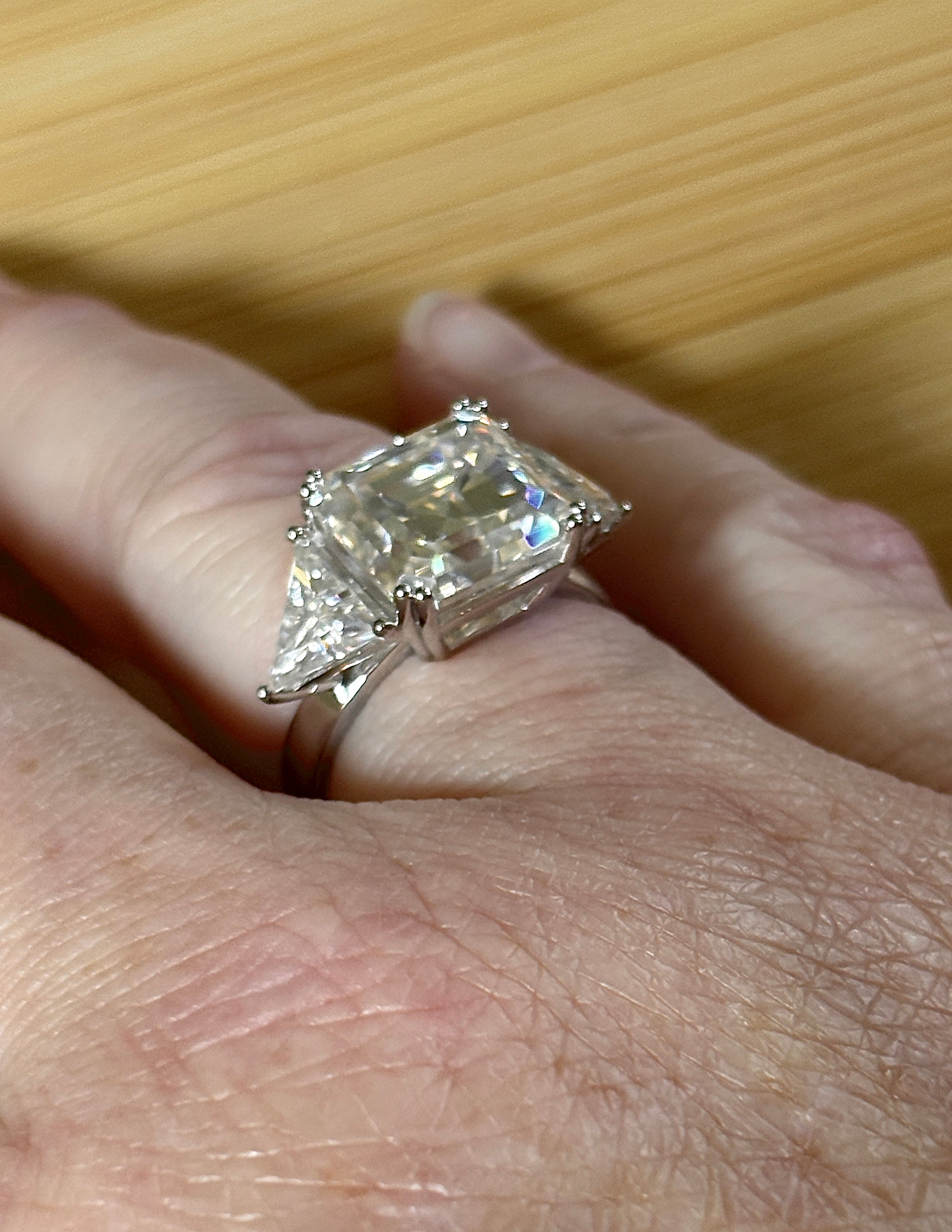 A 9.4cttw Moissanite statement ring with a 7ct Asscher-cut center stone and (2) 1.20ct Moissanite trillions, with bright 14k white rhodium!