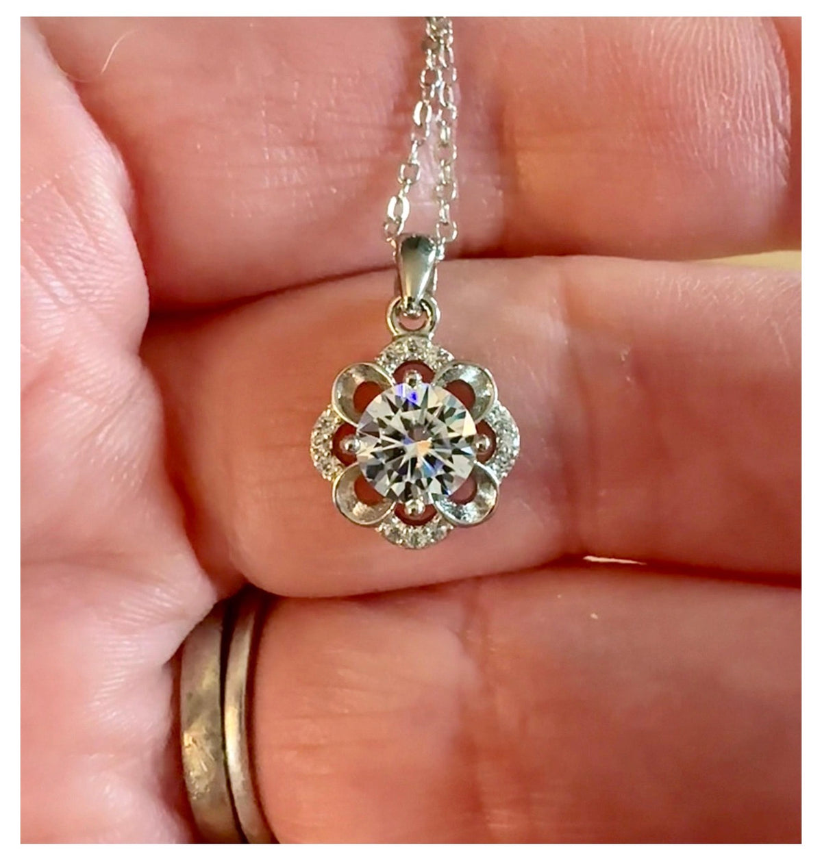 Moissanite necklace. With a floral motif, this pendant features a 1ct Moissanite nestled within alternating “petals” of silver and zircons!