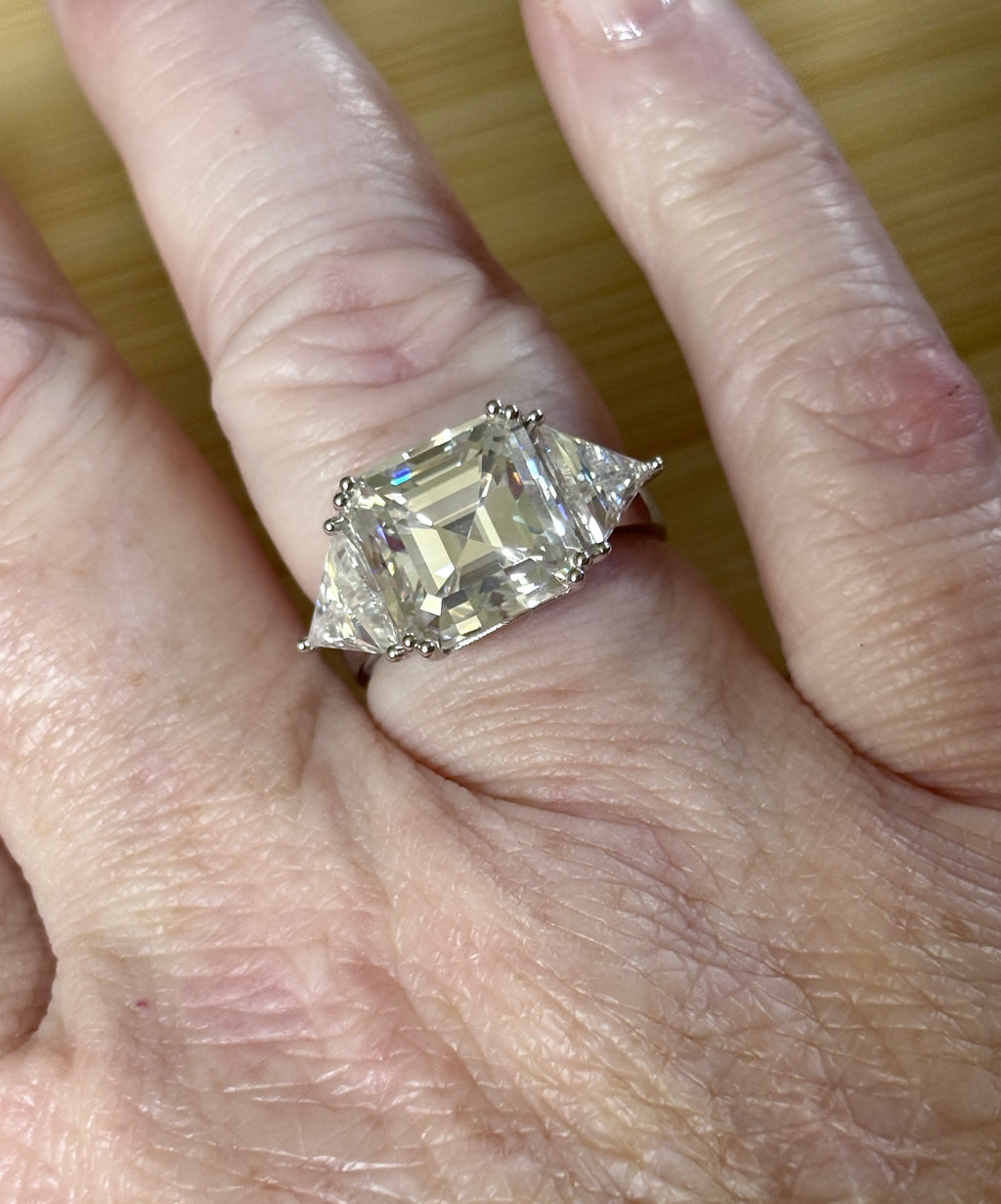 A 9.4cttw Moissanite statement ring with a 7ct Asscher-cut center stone and (2) 1.20ct Moissanite trillions, with bright 14k white rhodium!