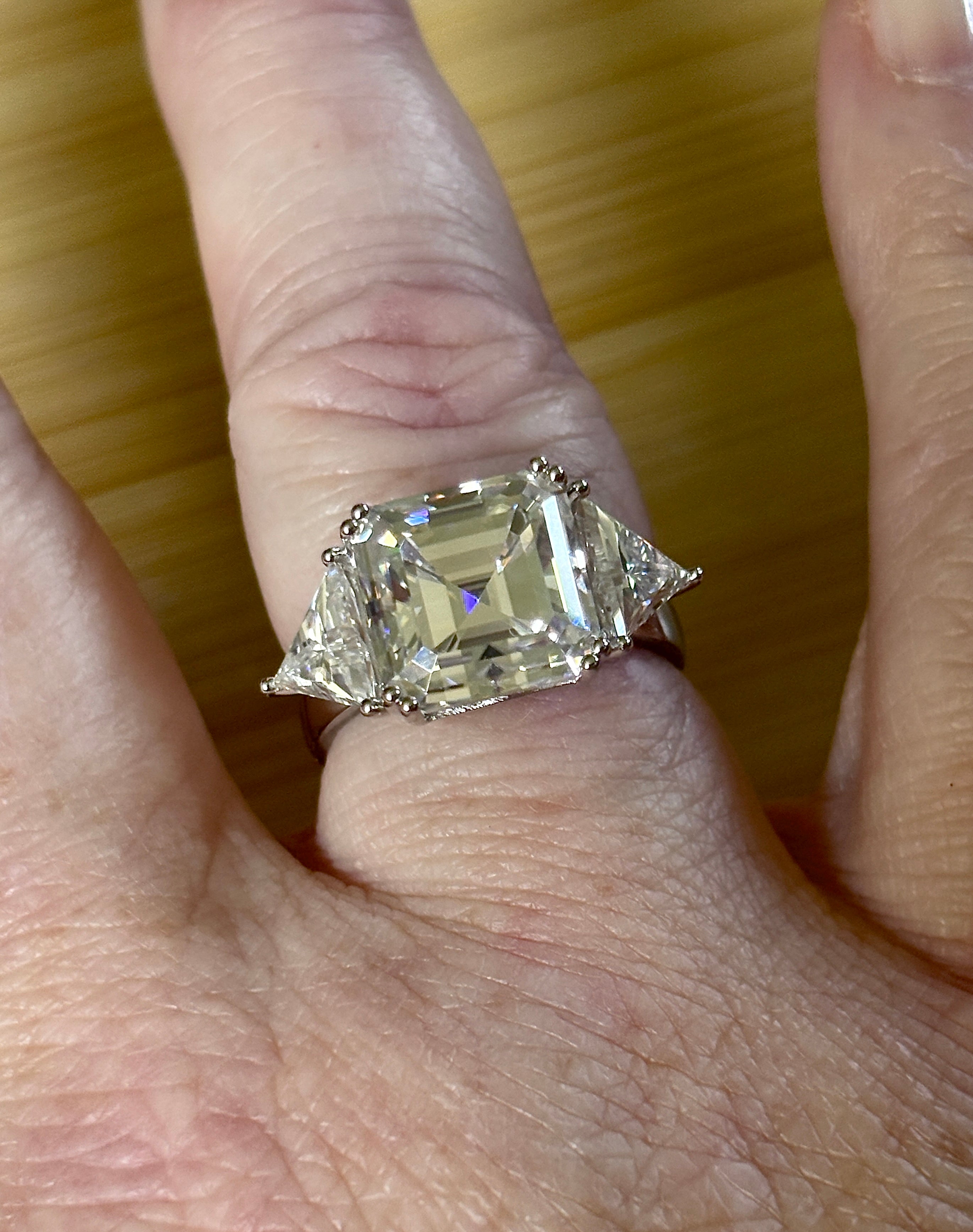 A 9.4cttw Moissanite statement ring with a 7ct Asscher-cut center stone and (2) 1.20ct Moissanite trillions, with bright 14k white rhodium!