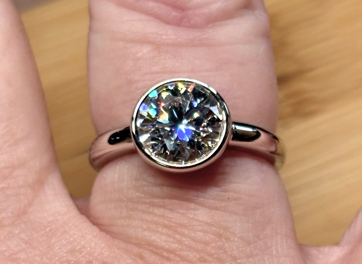 Moissanite solitaire. A 3ct certified round brilliant Moissanite in a weighty solid sterling silver bezel mounting with Seiko-electroplated 18k! A sleek, minimalist design!