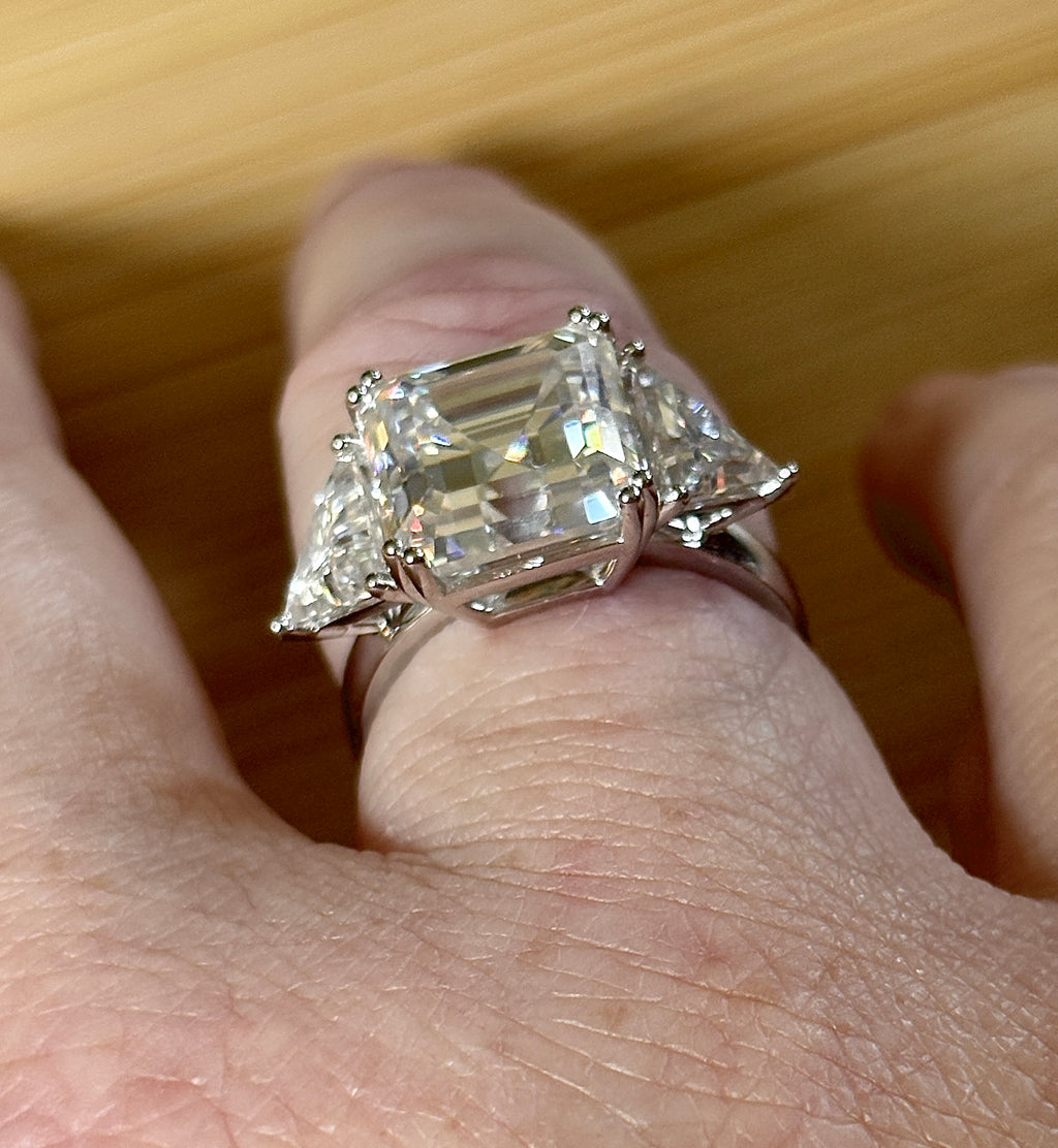 A 9.4cttw Moissanite statement ring with a 7ct Asscher-cut center stone and (2) 1.20ct Moissanite trillions, with bright 14k white rhodium!